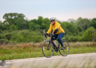 Bright woman cycling outdoors in green landscape wearing yellow jacket and helmet.