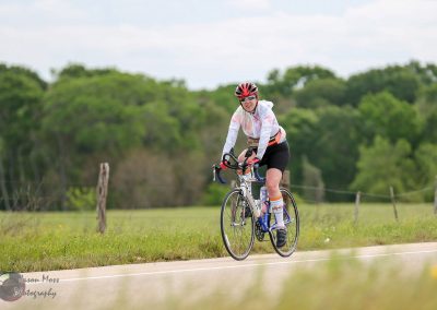Bright female cyclist riding road bike on countryside path, active outdoor biking adventure, bluebonnet express cyclist.