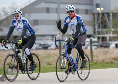 Pedestrians riding bikes in Bluebonnet Express cycling event, smiling and waving.