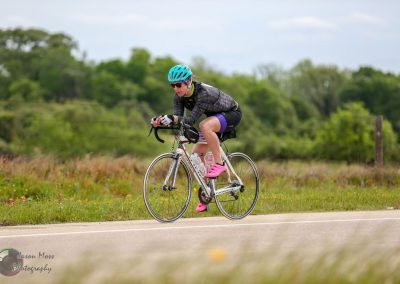 Cyclist riding a road bike on a scenic countryside route with greenery and open fields.