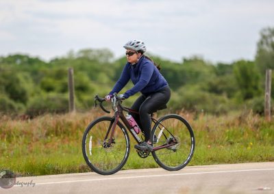 Bright female cyclist riding a road bike through scenic countryside during daytime.