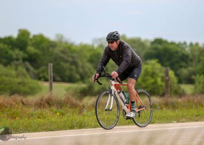 Vast bike ride outdoors on scenic Texas countryside road, cyclist wearing helmet and cycling gear.
