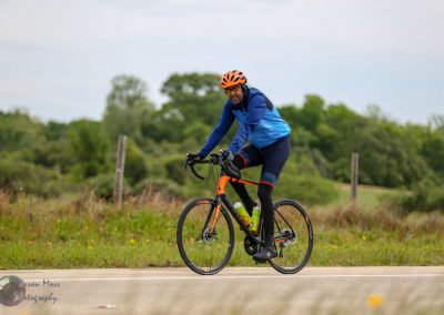 Bright blue cycling jersey with orange helmet on a road bike during outdoor ride.