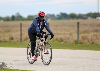 Cyclist riding a bicycle along a rural road in the Bluebonnet Express scene.