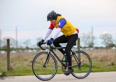 High-performance cyclist wearing a yellow, blue, and red jacket riding a black road bike on a paved path.