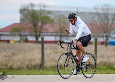 1. Cyclist wearing a black helmet and white shirt using a smartphone on a city bike ride.
