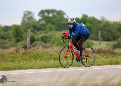 Extreme endurance cyclist riding a red BMC road bike on a scenic rural route.