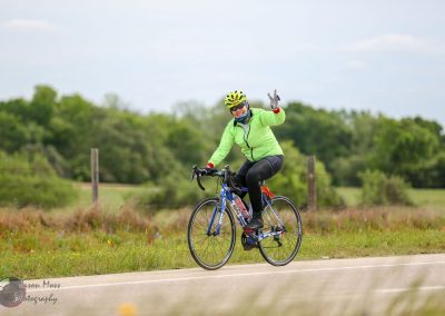 Vibrant cyclist riding Bluebonnet Express bike on rural road during daytime, outdoor biking adventure, Texas scenery.
