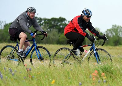 Hiker riding a blue gravel bike through a grassy field with wildflowers.