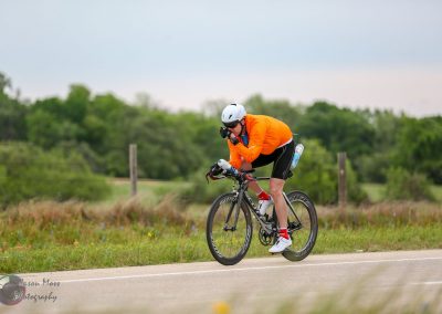 Bright orange cycling jersey with helmet on a scenic countryside road during daytime.