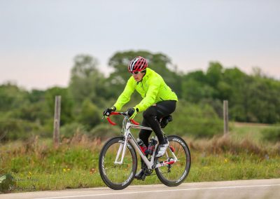 Bright neon yellow cycling jacket worn by cyclist riding on rural road against green landscape, promoting Bluebonnet Express.