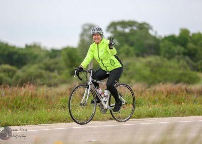 Bright yellow cycling jacket on woman riding bike through scenic outdoor landscape, Bluebonnet Express.