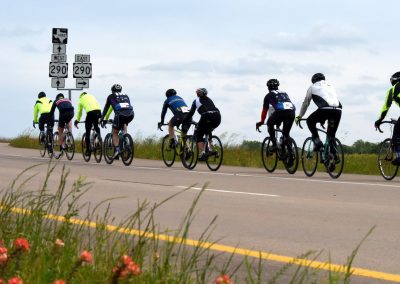 Group of cyclists riding on highway in daylight, Bluebonnet Express, outdoor biking, Texas scenery.