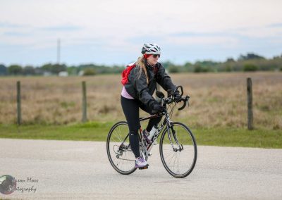 1. Woman riding a black road bike outdoors in casual cycling gear for Bluebonnet Express.