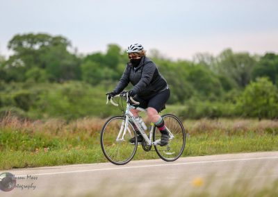 Bright woman cycling outdoors wearing safety gear on a scenic trail with greenery in the background.