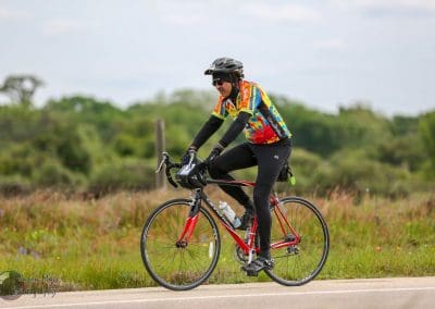 Vibrant cyclist wearing Bluebonnet Express jersey riding a red bike on scenic rural trail.