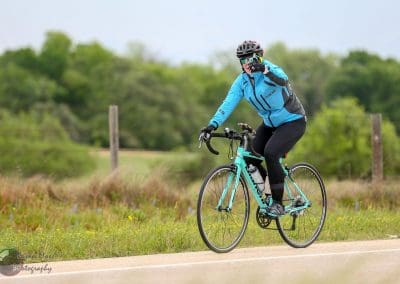 Cyclist riding a bike along a scenic rural trail during daytime with greenery in the background.