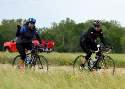 Brightly colored cyclists enjoying a scenic ride on Bluebonnet Express trail with a red pickup in the background, promoting Texas bike trail adventures.