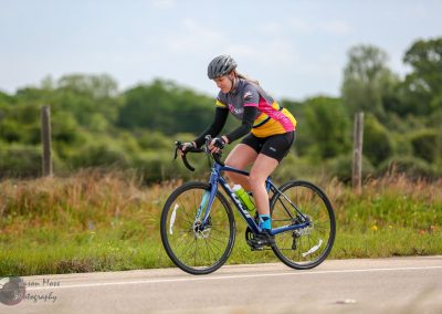 Female cyclist riding blue bike outdoors during daytime, promoting Bluebonnet Express cycling event.