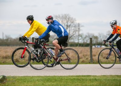 Brightly dressed cyclists riding bicycles outdoors on a paved trail during daytime.