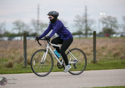 Bright woman riding a bicycle during daytime, wearing a helmet and sunglasses for safety and outdoor activity.