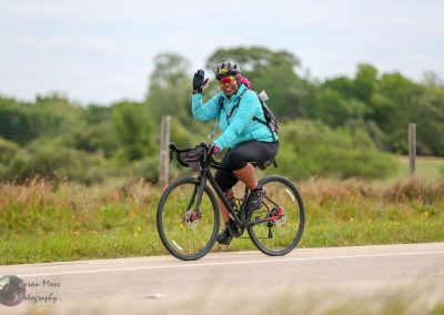 Bright female cyclist riding a bike on country road, emphasizing Bluebonnet Express cycling experience.