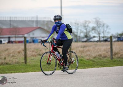 Bright blue and yellow cycling jersey on woman riding a red bike outdoors in daytime.
