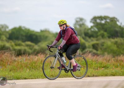 Vibrant female cyclist riding on scenic trail with lush greenery in the background.
