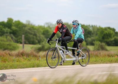 Bicycle built for two on scenic outdoor route with lush green landscape and cloudy sky.