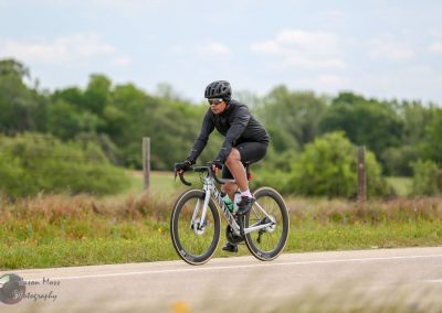 Wide-angle cyclist riding a mountain bike on open rural road near Texas Bluebonnet fields during daytime.