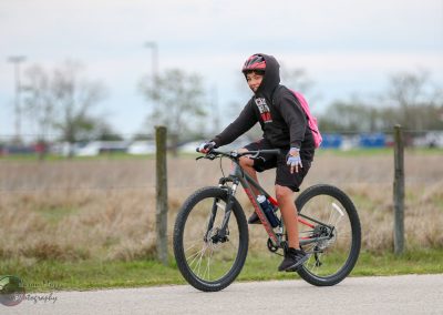Child riding a bike outdoors on a cloudy day, wearing safety gear and a backpack, enjoying a recreational activity.