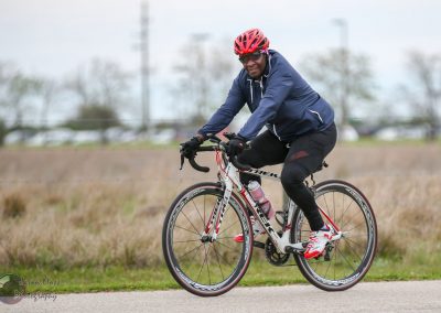 Man cycling outdoors on road in athletic gear for Bluebonnet Express event.