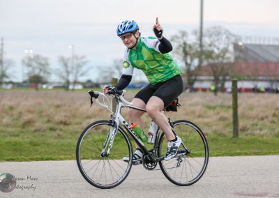 Man riding a bicycle during a cycling event on a cloudy day, promoting Bluebonnet Express bike rides for community fitness.