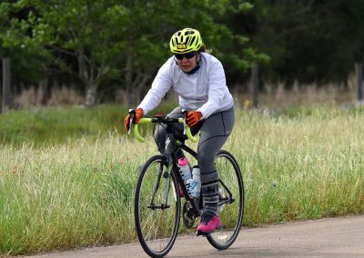 Vibrant female cyclist riding on scenic trail with lush greenery, showcasing Bluebonnet Express cycling adventure.