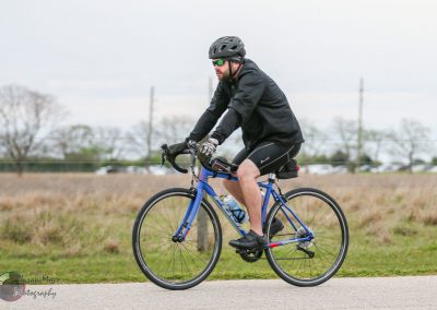 High-performance cyclist riding a road bike on a scenic trail with Bluebonnet Express branding.