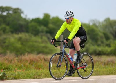 Bright yellow cycling jacket and black shorts on a male cyclist riding a road bike outdoors.