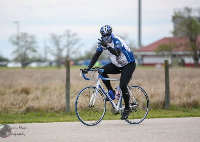 Bluebonnet express cyclist wearing helmet and cycling gear on a bike on a paved path outdoors.