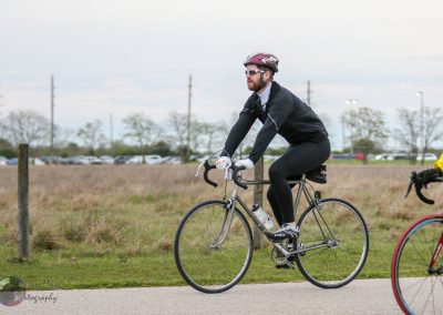 Bright male cyclist riding a bike outdoors on a paved trail in cloudy weather.