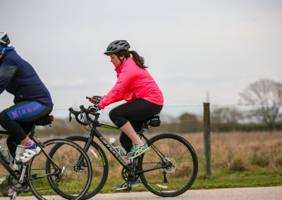 Comfortable woman riding a bike outdoors during daytime, wearing a pink jacket and helmet, on a scenic trail.