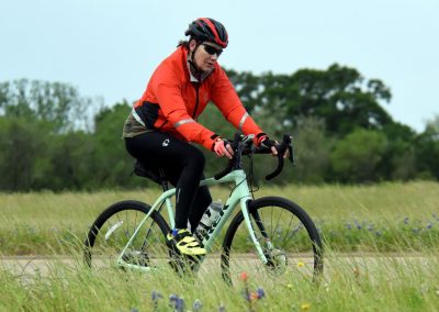 Bright, professional cyclist riding gravel bike in countryside, promoting Bluebonnet Express bike services.