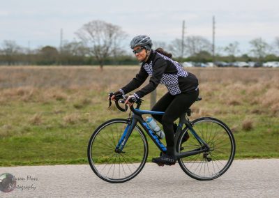 Fast woman riding a blue Trek road bike in an open outdoor area during daytime for Bluebonnet Express event.