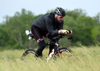 High-performance cyclist riding a time-trial bike on a grassy trail; outdoor sports and triathlon gear.