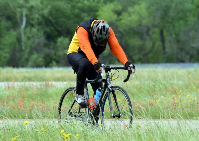 Vibrant cyclist on mountain bike riding through a lush green field with wildflowers during daytime.
