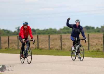 Happy cyclists riding on a scenic bike path with open fields and a cloudy sky.