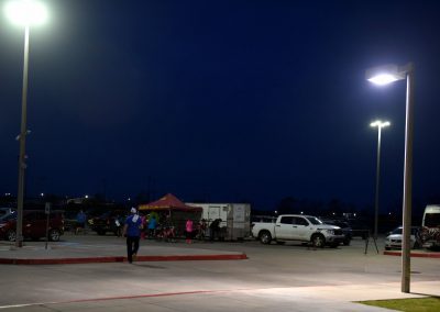 Bright outdoor parking lot illuminated at night with people gathering under a red tent, promoting Bluebonnet Express bike services.