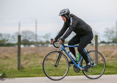 Bright blue bike on outdoor cycling trail, cyclist in black jacket and helmet, enjoying a scenic ride.