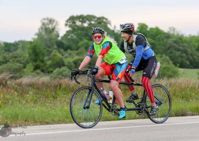 Bright, smiling cyclists on a tandem bike enjoying a sunny outdoor ride in nature.