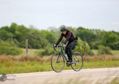Bright woman cyclist wearing helmet on rural road with greenery, promoting Bluebonnet Express bike service.