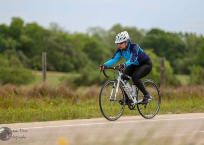 Light blue and black cyclist riding on a rural road during cloudy weather.