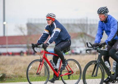 Energetic cyclists riding bikes outdoors on a cloudy day with open field background.